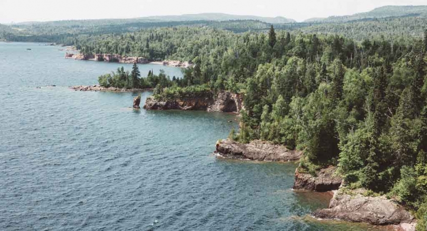 from a high vantage point, a the shore of a blue lake collides with a rocky shore lined with green trees